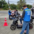 Dois autopropelidos estão parados em um espaço aberto. Neles, há pessoas sentadas conversando com outras pessoas vestidas com um colete azul de educação para o trânsito