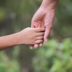Imagem mostra parcialmente o braço de um adulto segurando a mão de uma criança