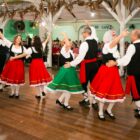 Quatro duplas, três formadas por homem e mulher e outra por duas mulheres, estão usando figurinos de dança e dançando em um salão de baile