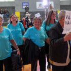 Mulheres idosas vestidas de azul sorriem para a foto enquanto caminham por um ginásio de esportes