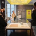 Imagem mostra mulher apresentando a sala de um museu a um grupo de homens