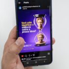 Mão masculina e branca segura celular. Na tela, há um post da Prefeitura de Joinville na cor roxa, com uma ampulheta, que fala sobre violência contra a pessoa idosa