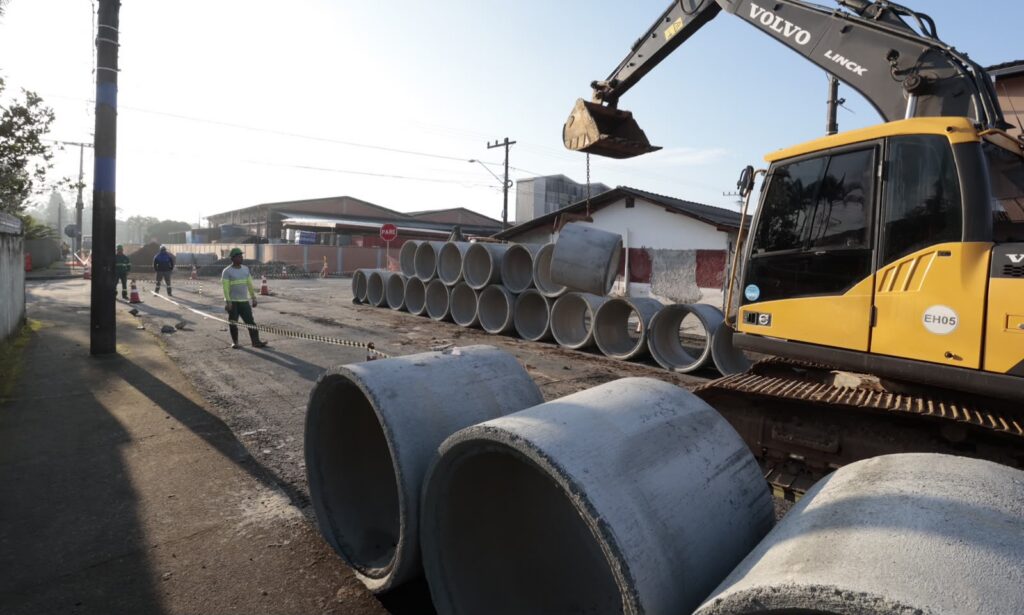Máquina em via com tubos empilhados e operários
