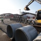 Máquina em via com tubos empilhados e operários