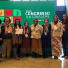 Homens e mulheres estão em pé, em frente a um painel com a escrita Congresso Conasems. Eles posam e sorriem para a foto