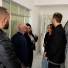 Duas mulheres e três homens estão conversando em um imóvel, ao lado de uma van