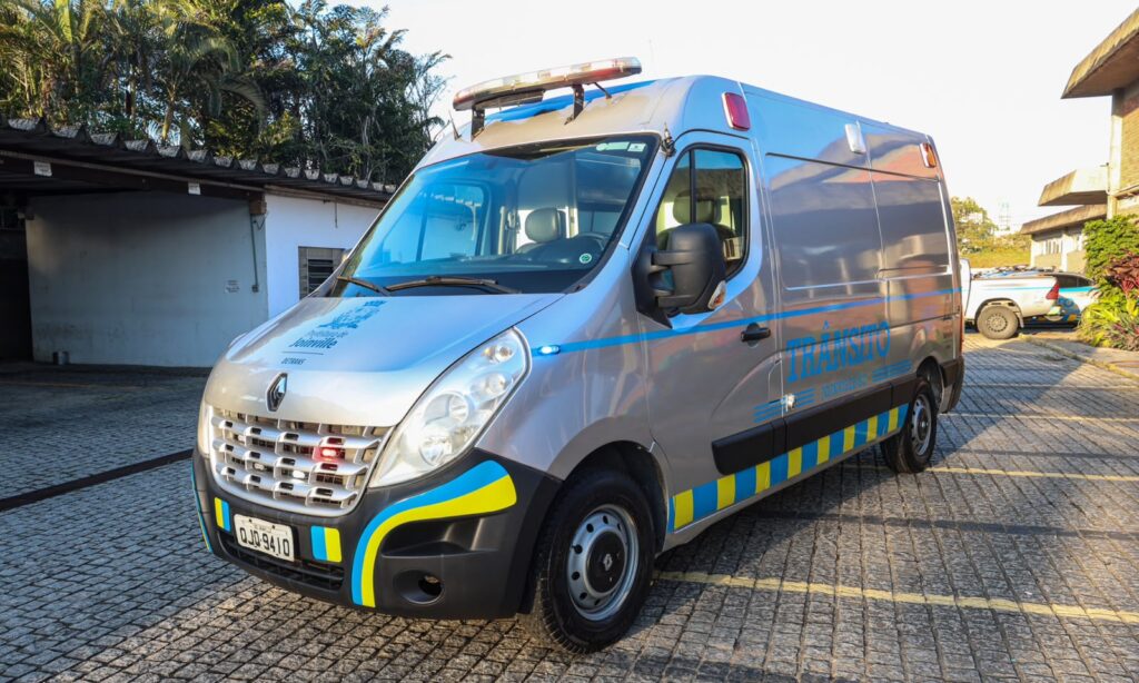 Van prata com plotagem em tons de amarelo e azul está estacionada em um pátio