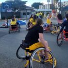 Crianças e adolescentes estão em cadeiras de rodas, praticando o basquete em cadeira de rodas em uma área aberta