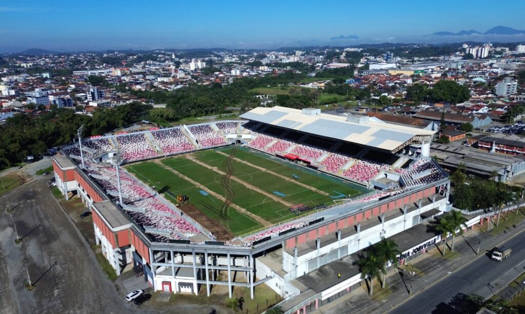 Imagem aérea mostra estádio de futebol que passa por troca de gramado, com presença de valas