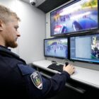 Guarda municipal está dentro de um ônibus equipado onde observa três monitores que mostram imagens de monitoramento de ruas