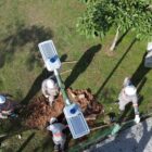 Imagem aérea mostra homens uniformizados e com capacete trabalhando no chão próximos a um poste