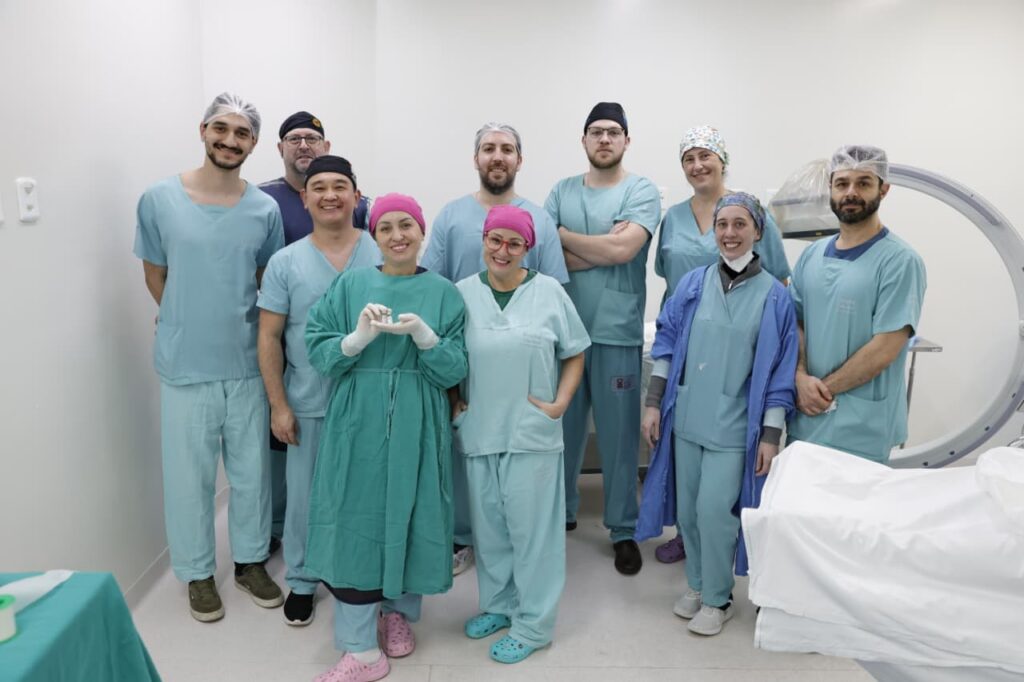 Homens e mulheres com roupas hospitalares posam para foto. Uma das mulheres segura dois frascos na mão