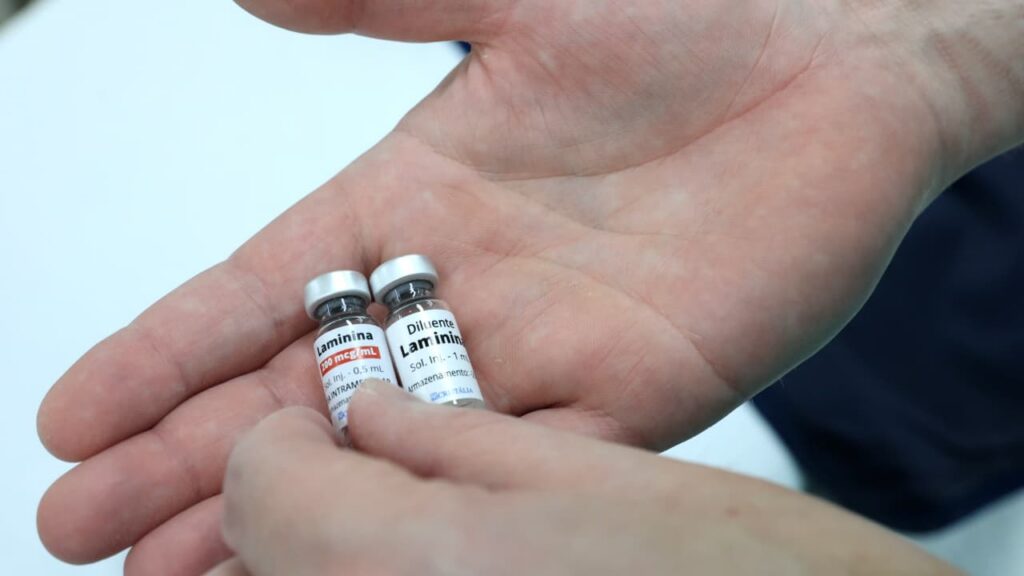 Mão segura dois pequenos frascos com rótulos com a palavra laminina