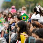 Pessoas segurando bandeirinhas assistem ao desfile