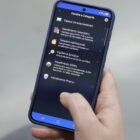 Imagem mostra mão feminina, segurando um celular. Na tela, há uma página do aplicativo Joinville Fácil que permite fazer agendamentos
