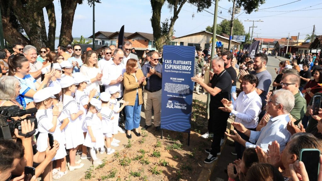 Homens, mulheres e crianças aplaudem e sorriem. Perto deles há uma placa que marca a inauguração do Cais Flutuante do Espinheiros