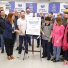 Homens e mulheres estão em pé e olham para uma placa de metal exposta em um tripé que marca a entrega da ampliação e reforma da escola
