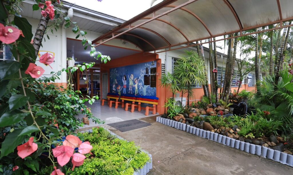 Imagem mostra espaço da Escola Municipal Adolpho Bartsch com paredes coloridas, flores e outros tipos de vegetação