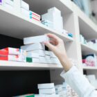 Mão feminina pega uma caixa de medicamento em uma prateleira repleta de outros medicamentos