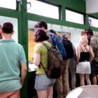 Mulheres e homens estão de costas para a câmera, observando a vitrine com artefatos do povo sambaquiano em um museu