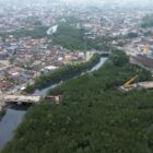 Imagem aérea mostra obras da Ponte Anêmonas. Há estruturas construídas em ambos os lados de uma área de vegetação por onde passa um rio. No entorno desta área, há ruas e residências.