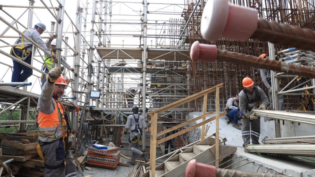 Imagem das obras da Ponte Joinville mostram trabalhadores uniformizados e de capacete trabalhando em uma estrutura repleta de ferros