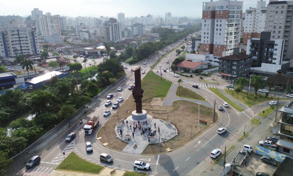 Imagem aérea mostra praça onde está instalado um grande monumento que mostra uma mão segurando a outra, como se uma pessoa estivesse ajudando a outra a se reerguer