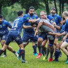 Diversos homens com uniforme azul jogam uma partida de rugby em um dia de chuva