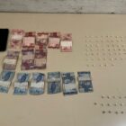 Imagem mostra notas de dinheiro em real, três celulares, um maço de cigarro e pedras de crack em cima de uma mesa
