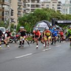 Dezenas de homens e mulheres praticam patinação em linha em uma rua asfaltada com prédios e vegetação no entorno