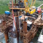Imagem mostra escavação de estacas na Ponte Joinville. A imagem aérea mostra uma área com ferragens, máquinas e outros equipamentos