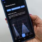 Mão feminina com unhas rosas segura um celular que mostra a imagem de uma tábua de marés