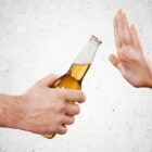 Imagem mostra duas mãos de pessoas diferentes de frente uma para a outra: uma delas oferece uma garrafa de cerveja, enquanto a outra recusa.