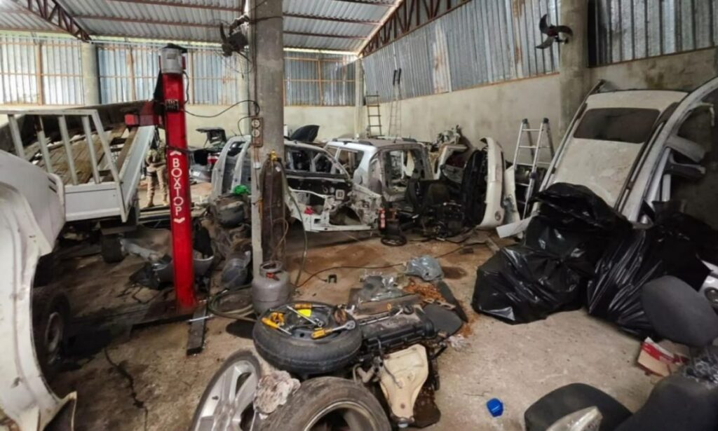 Foto mostra um grande galpão fechado com peças de carro desmontadas