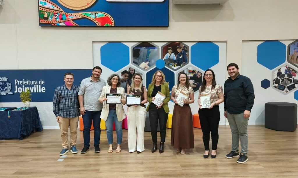 Foto mostra oito pessoas, entre homens e mulheres, em pé, com medalhas no pescoço, posando para a foto.
