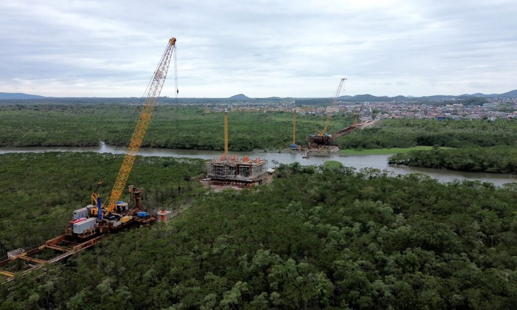 Foto aérea mostra três partes da obra da Ponte Joinville em meio ao rio e à vegetação