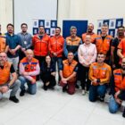 Foto mostra dezenas de pessoas posando para a câmera. Há uma fila de pessoas em pé e outra de pessoas agachadas à frente. A maioria das pessoas usa coletes laranja da Defesa Civil.