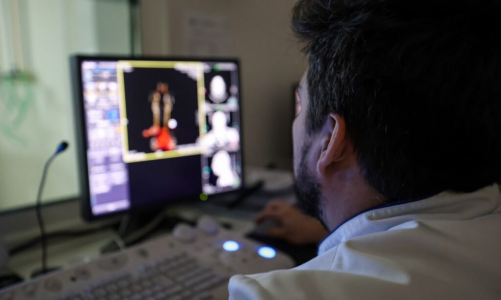 Foto mostra parcialmente o rosto de um homem observando uma tela de computador que mostra resultados de exame