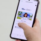 Foto mostra mão branca feminina segurando um celular na página do programa Saúde Conectada, que oferece videoconsulta em Joinville